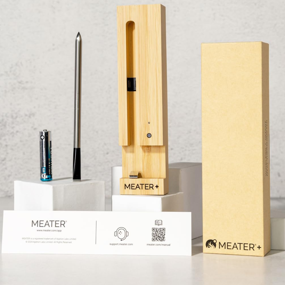 A MEATER Wireless Smart Meat Thermometer kit, featuring a bamboo charging station, a metal probe, a battery, and an instruction card, displayed on a neutral background.