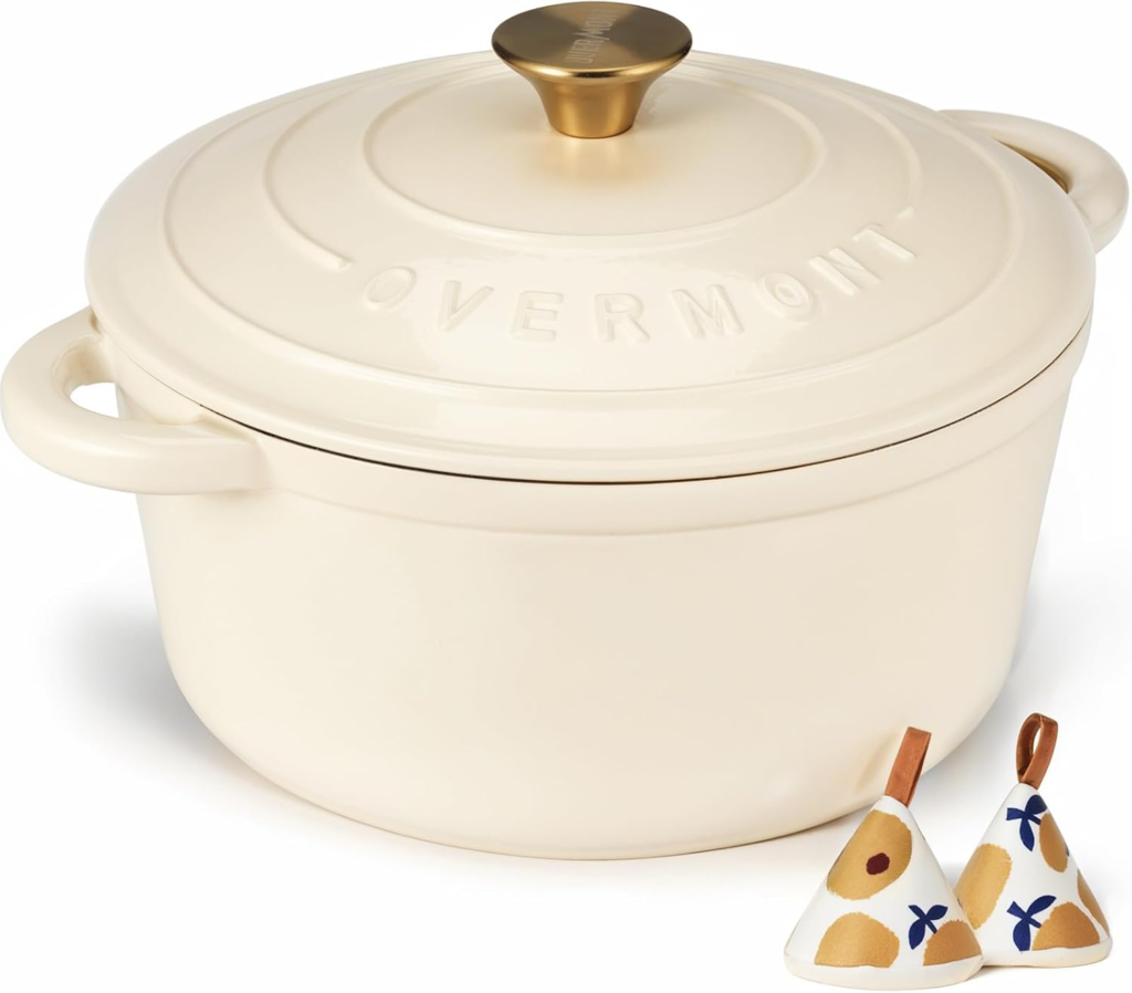 Enameled cast iron Dutch oven in cream color with a matching lid and decorative kitchen accessories.